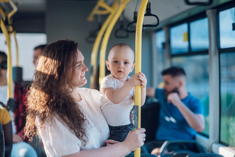 Mother holding her baby while standing on a city bus, both looking content during their public transport ride