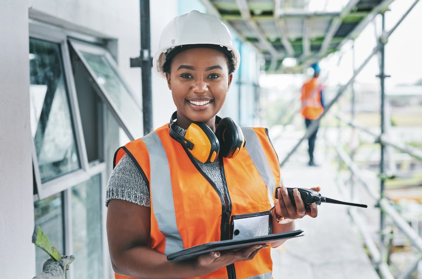 Happy construction worker in a hard hat smiling while holding a power tool at an active building site