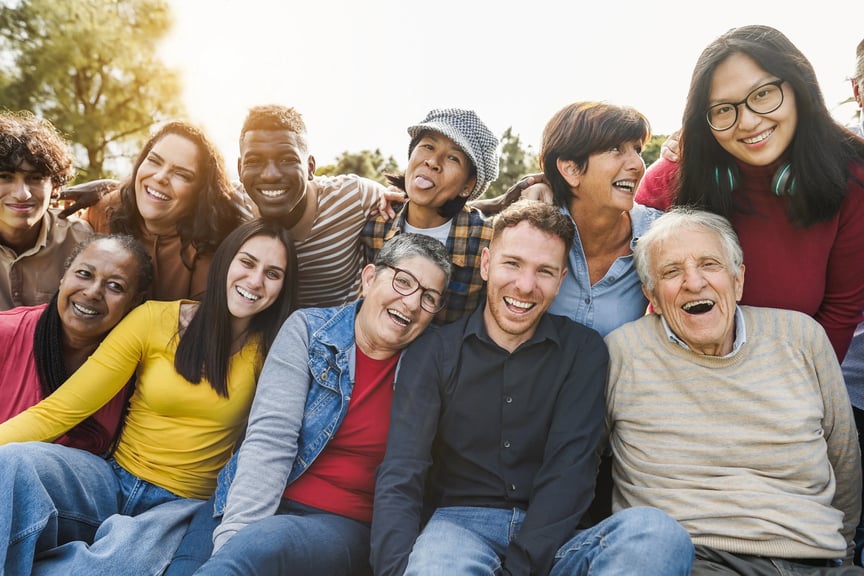 Group of diverse people of different ages and backgrounds smiling together outdoors, representing community and inclusion