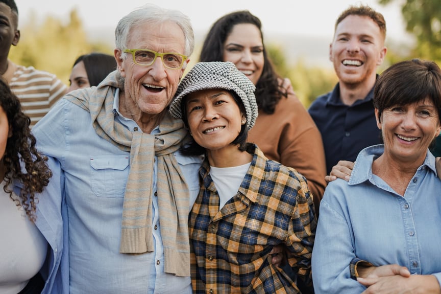 Diverse group of smiling adults posing together outdoors, showcasing multigenerational community and friendship