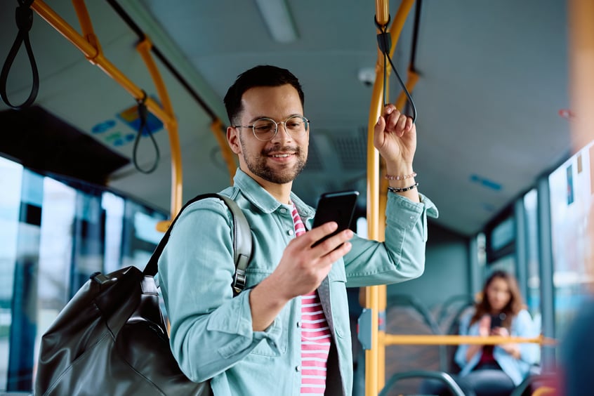 Smiling man standing on a city bus holding a smartphone and looking at the screen during his commute