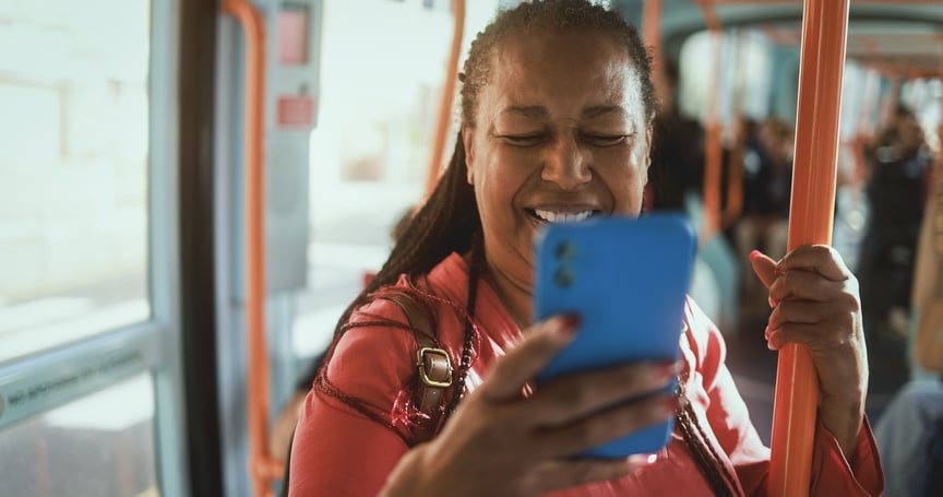 Smiling woman on a bus holding a smartphone and laughing while checking her messages