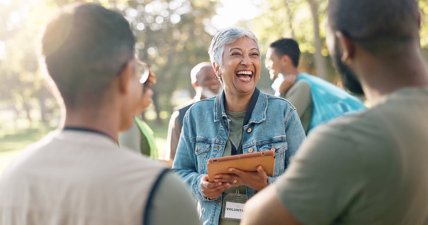 Smiling woman volunteer holding a tablet and laughing while talking with her team during a community event outdoors