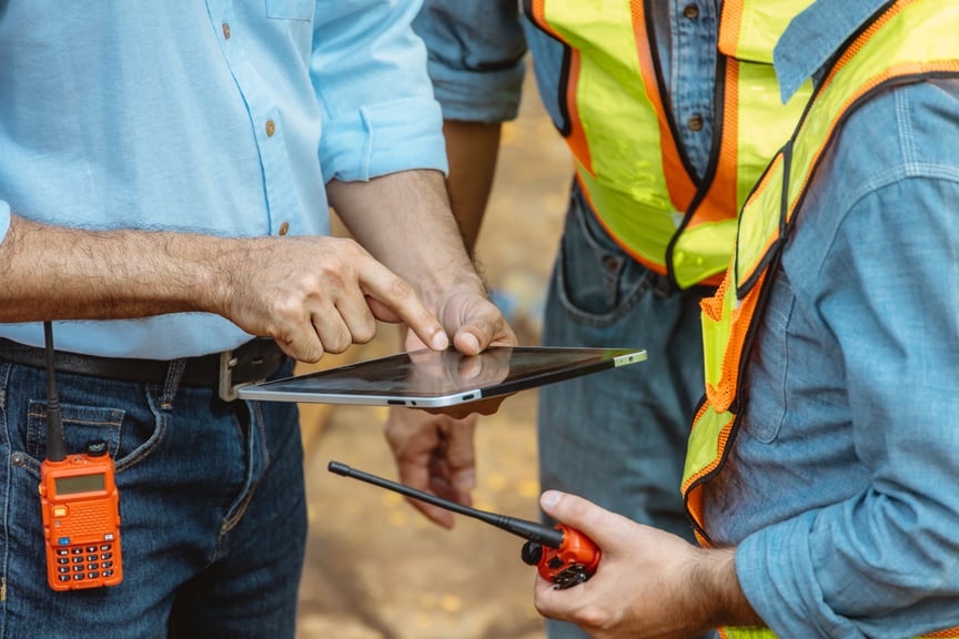 Construction engineers using a digital tablet to review site plans while communicating with walkie-talkies at a building site
