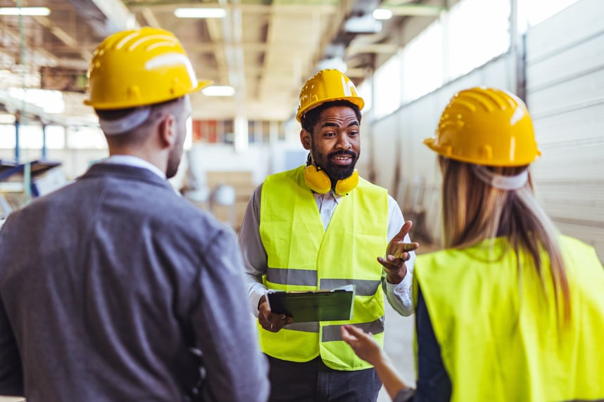 Engineer wearing a yellow safety helmet and reflective vest leading a discussion with colleagues during a site inspection inside an industrial facility